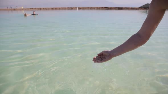 Man's hand touching sea water. Woman swimming at the background. The Dead Sea, Israel alt