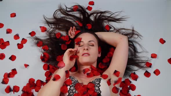 An attractive woman laying on the floor looking sexy with red rose petals falling all around her
