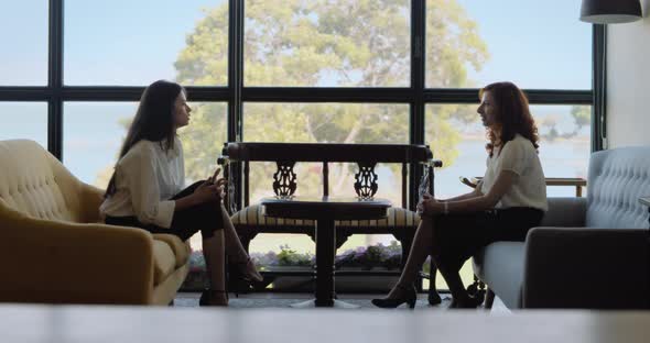 Two young women having a friendly conversation during a business meeting in a hotel lobby. alt