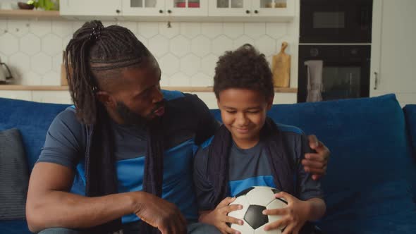 Caring African Father Cheering Up Upset Son with Soccer Ball After Team Defeat alt