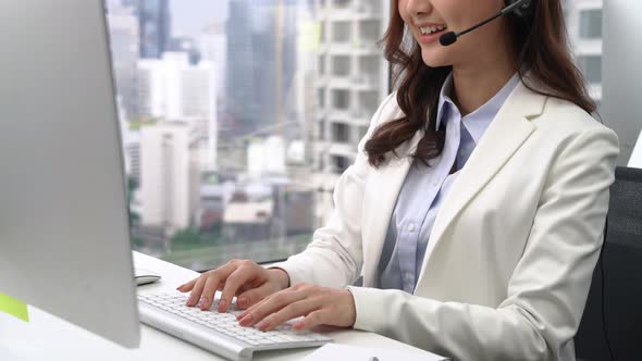 Woman operator typing on computer keyboard and talking with customer on microphone headset