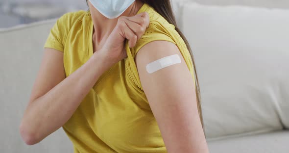 Midsection of asian woman in face mask sitting on sofa showing arm with ...