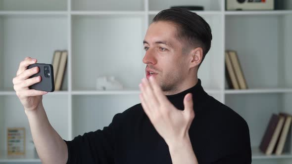 Portrait of Happy Man Making Facetime Video Calling with Smartphone at Modern Office Waving at alt