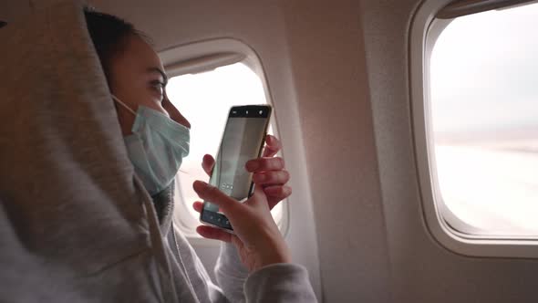 Happy Woman Tourist in Medical Face Mask Looking at Aircraft Window in Airplane Cabin alt