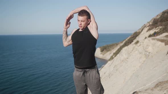 Tattooed Muscular Man Does Workout Outdoors at Sunny Day on Top of Mountain alt