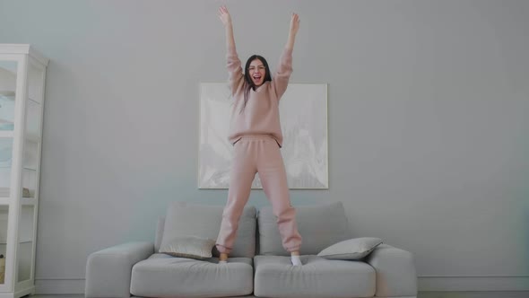 Funny young caucasian woman with glasses happily dancing and jumping on sofa.