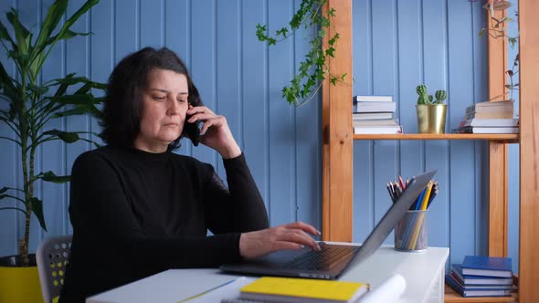 Middleaged Woman is on the Phone and Working in a Home Office