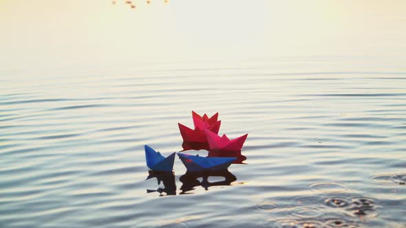 Toy paper boats on the surface water at sunset. Colored paper ships in the water alt