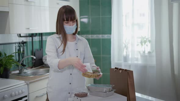 Pandemic, Young Woman in Medical Mask Treats Food Delivered Home with an Antiseptic To Protect alt