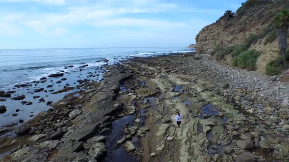 Tracking shot of a young man running on a rocky ocean beach shoreline alt