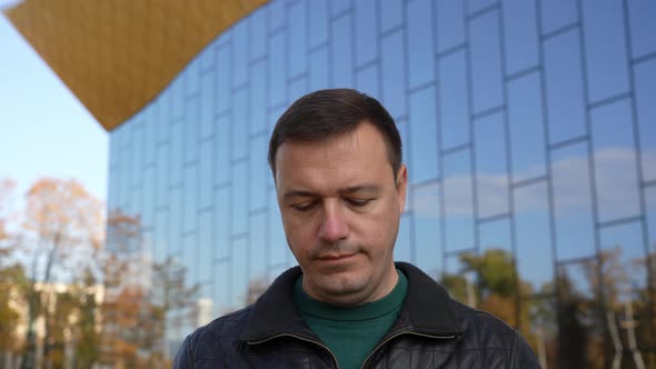 Calm Millennial Man Puts on a Medical Mask While Looking at the Camera at City Street alt