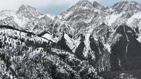 Bird's-eye view camera shoots snowy rocks and forest in snowfall in Kananaskis, Alberta, Canada alt
