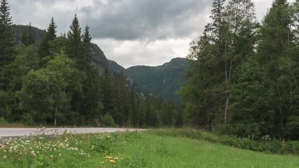 Mountain forest road, time lapse of cars driving on overcast day, zoom out alt