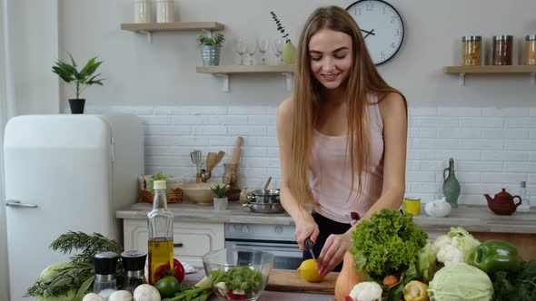 Girl Coming To Table with Juicy Lemon. Young Woman Cutting Fresh Fruit with Knife and Smiling alt
