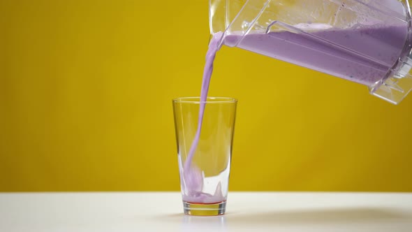 Pouring of Healthful Vitamin Purple Cocktail in Glass at Yellow Background in Slow Motion alt
