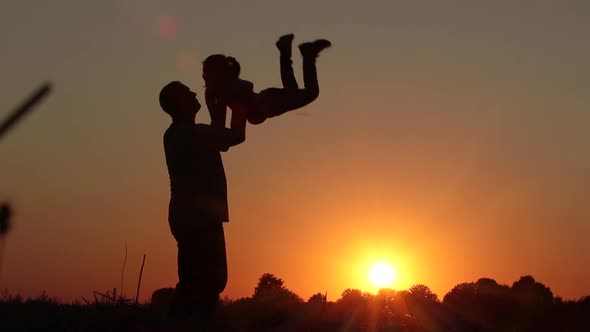 SLOW MOTION: Dad throws a little daughter in the field at sunset. Silhouettes of people.