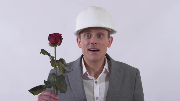 Young Man in Construction Hat and Classical Suite Give a Long Red Rose in White Background alt