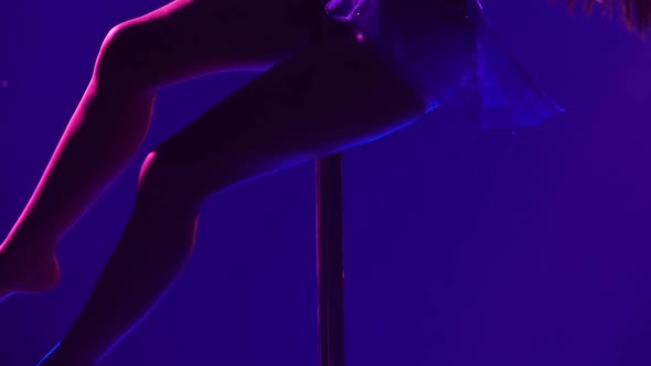 Athletic Flexible Woman Rotates on a Pole in a Dark Studio with Blue Neon Lights alt