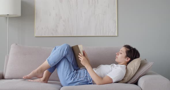 Caucasian Girl Reading Paper Book Relaxing at Home Apartment Natural Light