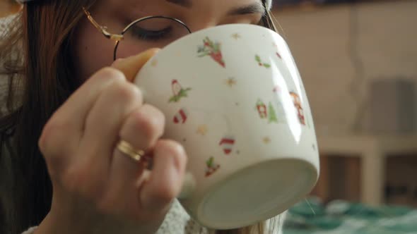 A Girl in a Santa Claus Hat Drinks Cocoa From a Cup