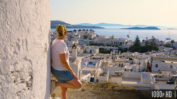 Female Tourist Looking at the View of Windmills and Mykonos Town at Sunset, Greece alt