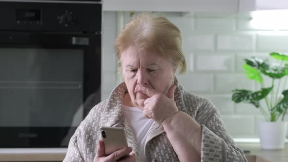 Sad Frustrated 70 Years Elderly Woman at Home Looking at Phone Seeing Bad News or Photos Feels alt