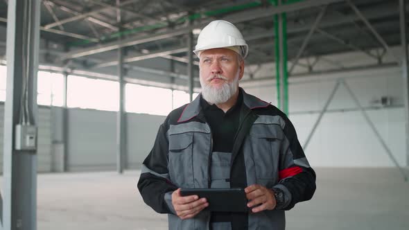 Portrait of Adult Grayhaired Man Technical Engineer Stands and Uses a Screen Tablet Perform a alt