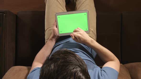 Young adult man with a tablet PC (green screen) on a sofa at home