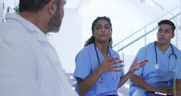 Asian female doctor sitting and discussing with diverse male colleagues at hospital staff meeting alt
