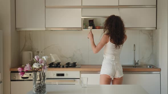 A Young Woman is Taking a Bag of Tea From the Shelf alt