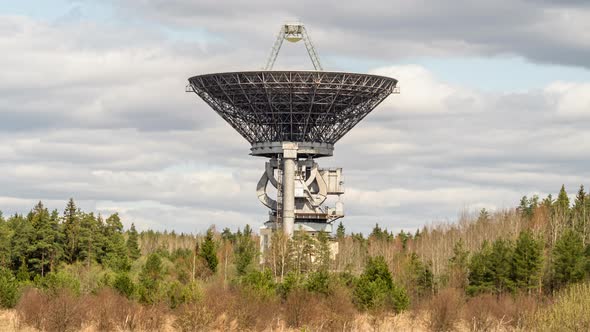 A radio telescope above forest in front of coudy sky alt