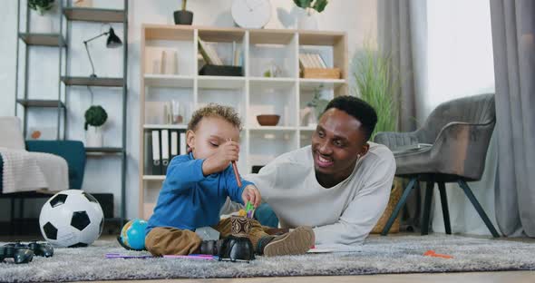 Man Lying on the Floor and Helping His Cute Baby Boy to Gether Coloured Pens alt