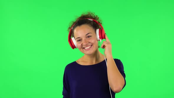 Portrait of Curly Woman Dancing and Enjoying Music in Big Red Headphones. Green Screen alt