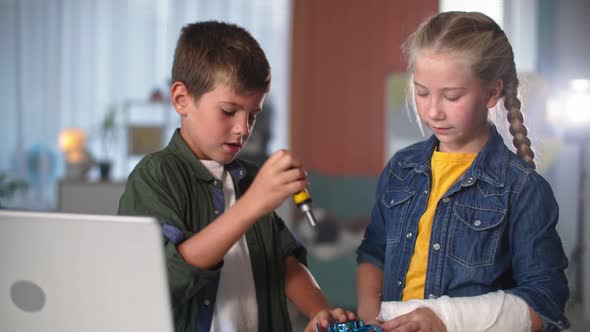 Smart Kids Repair Mini Quadcopter with Instruments Near Laptop Beautiful Girl with a Plaster Cast on alt