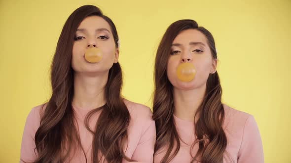 Twin Girls Blowing Chewing Gum Into Bubbles alt