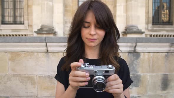 Young Woman Making Photo Rewinding a Film Camera on Background of Old European City
