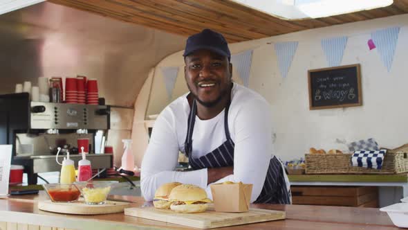 Portrait of african american man wearing apron smiling while standing in the food truck alt