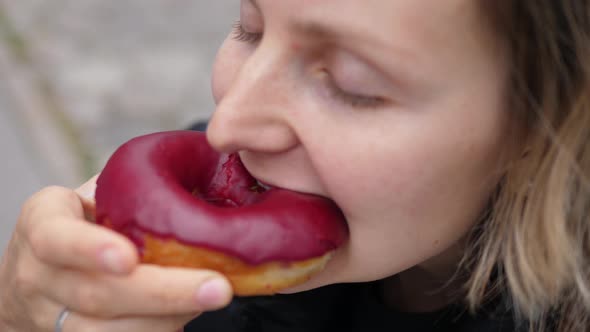 Close Up of a Hungry Woman Taking a Bite of Berry Vegan Doughnut with Her Eyes Closed alt