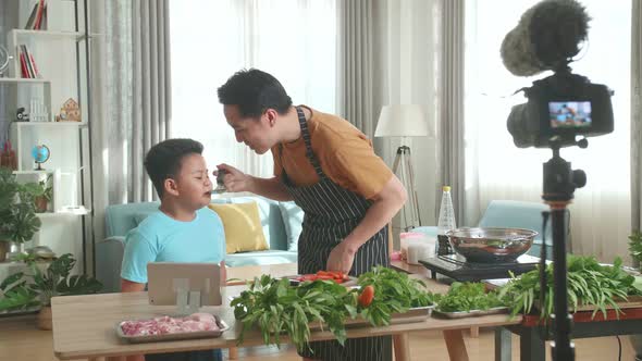 Asian Father And Son Streaming Live Video With Camera While Cooking At Home, Funny Food Tasting alt