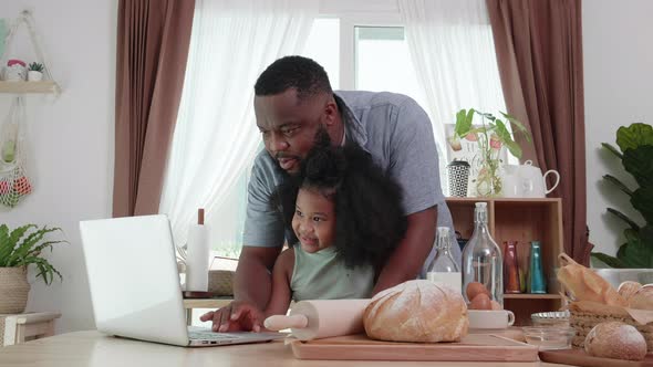 Love moment. African American dad helping daughter to use laptop at the home kitchen table