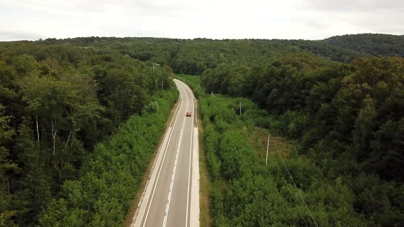 Orange SUV Car Driving on a Rural Road in the Mountains and Forest at Summer Sunny Day - Drone Point alt