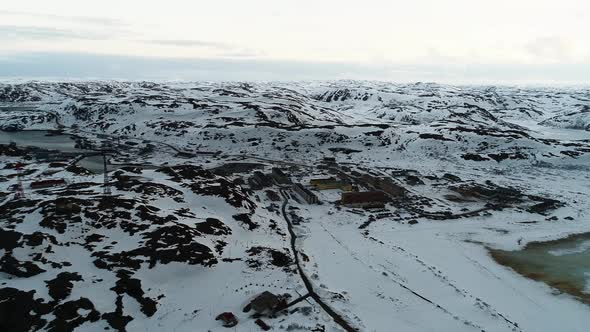 The Drone Flies Over a Small Northern Town Surrounded By Snowcovered Cliffs