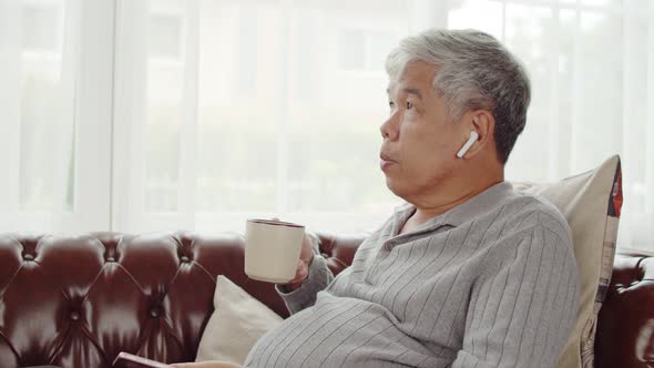 Senior man use wireless earphone listening music and drink coffee alt