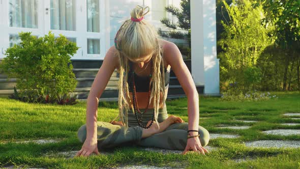 Woman Makes Belly Vacuum Exercise Sitting on the Lawn on the Backyard of House