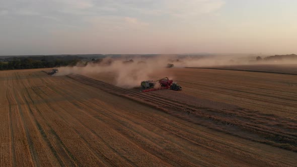 Aerial drone shot: combine harvesting wheat pouring harvested wheat into tractor tipper. alt