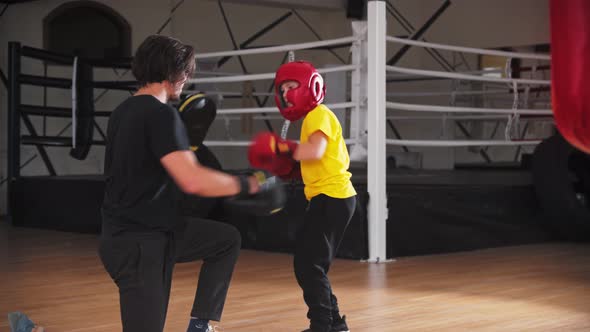 Little Smiling Boy in Protective Helmet Doing Boxing with a Coach alt