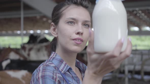 Portrait of Young Female Worker on the Cow Farm Checking Quality of Milk in the Bottle Close-up alt