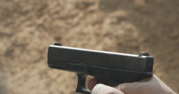 Slow motion of a man firing a hand gun in a firing range with cartridge flying away alt