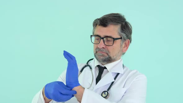 Senior Doctor in a Protective Mask Puts on Medical Gloves on Blue Background alt