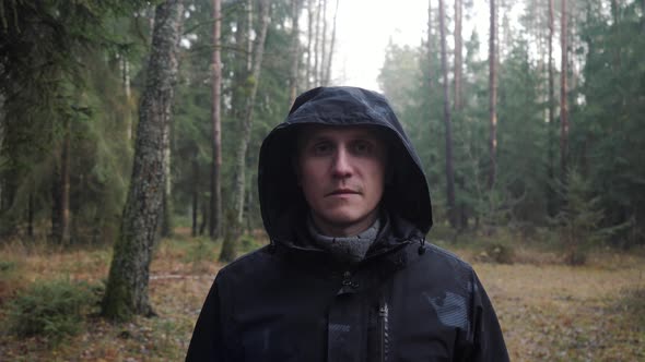Portrait of a Man in Warm Clothes with a Hood on His Head Standing in the Woods
